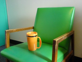 Orange mugg på grön stol med turkos dörr i bakgrunden